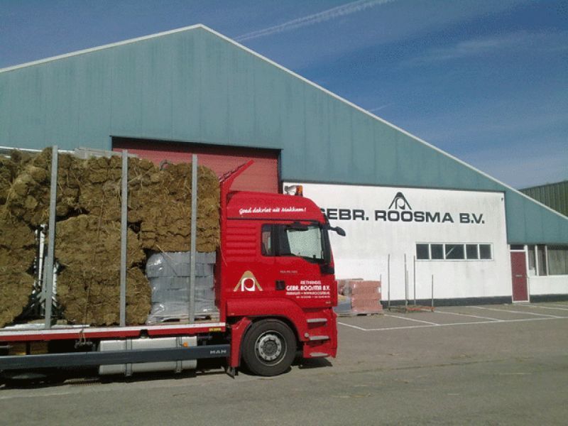 Rode vrachtwagen geladen met materiaal voor een rieten dak met daarop