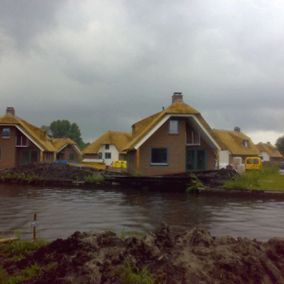 Huizen met rieten daken langs een kanaal onder een bewolkte hemel.