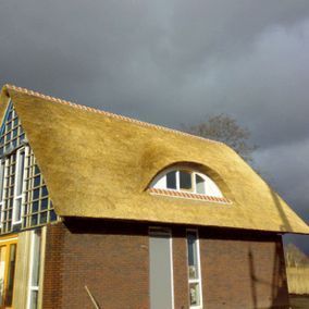 Rieten dak op een modern bakstenen gebouw, met een boograam en een bewolkte lucht.