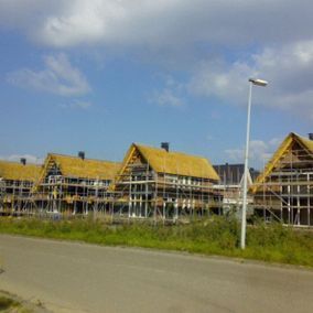 Huizen in aanbouw, steigers zichtbaar, rieten daken, blauwe lucht.
