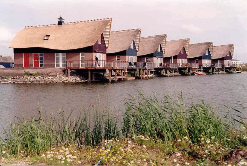 Een rij huizen op palen boven het water, met rieten daken en kleurrijke gevelbekleding.