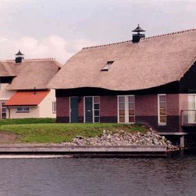 Huizen met rieten daken aan het water, bakstenen en witte buitenkant, groene gazons.