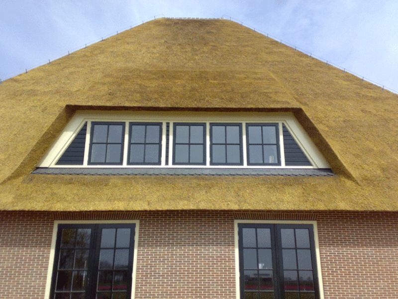 Close-up van een huis met een rieten dak, bakstenen gevel en ramen met zwarte kozijnen.