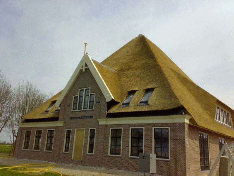 Bakstenen huis met een rieten dak, dakkapellen en een hoog, puntig dak.