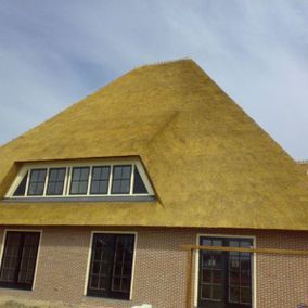 Een huis met een rieten dak, bakstenen muren en ramen tegen een blauwe lucht.
