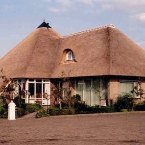 Huis met rieten dak, beige bakstenen buitenkant, boograam en aangelegde tuin.