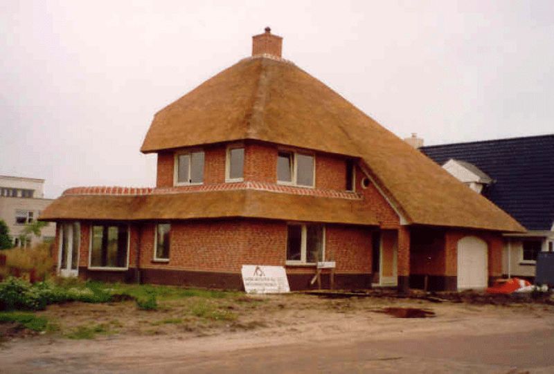 Bakstenen huis met twee verdiepingen en een rieten dak. Buitenfoto met bewolkte lucht.