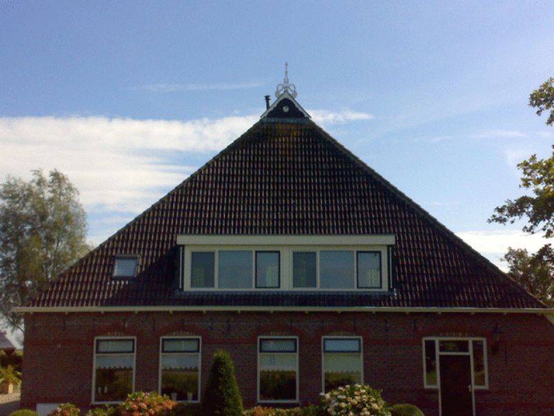 Bakstenen gebouw met een groot driehoekig dak en meerdere ramen, onder een blauwe lucht.