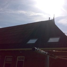Een donker dak met twee dakramen, een bakstenen gebouw onder een zonnige hemel.