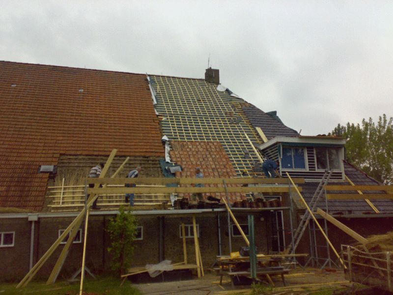 Dak van een gebouw in aanbouw, gedeeltelijk betegeld, arbeiders op steigers.