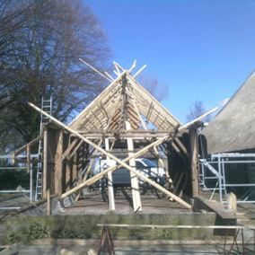 Houten frame van een gebouw in aanbouw, met steigers, tegen een helderblauwe lucht.