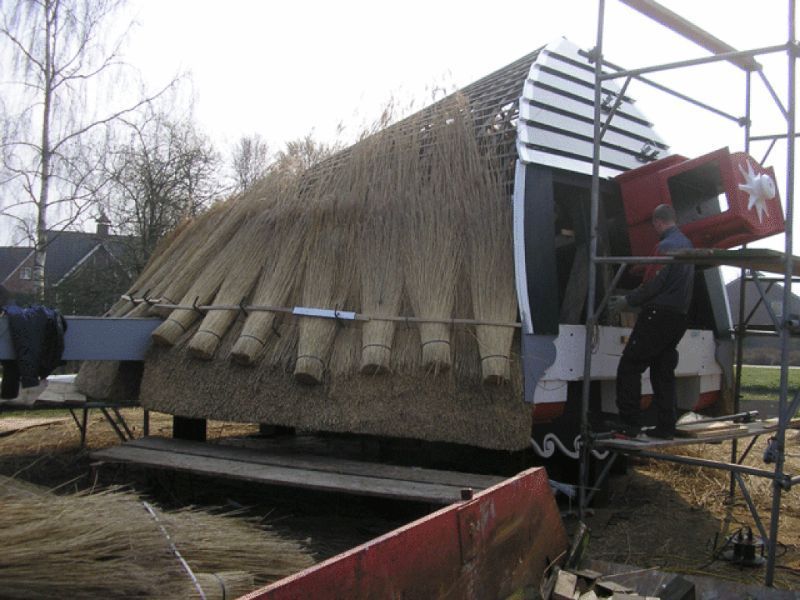 Er wordt een rieten dak op een gebouw geplaatst. Een man staat op een steiger.
