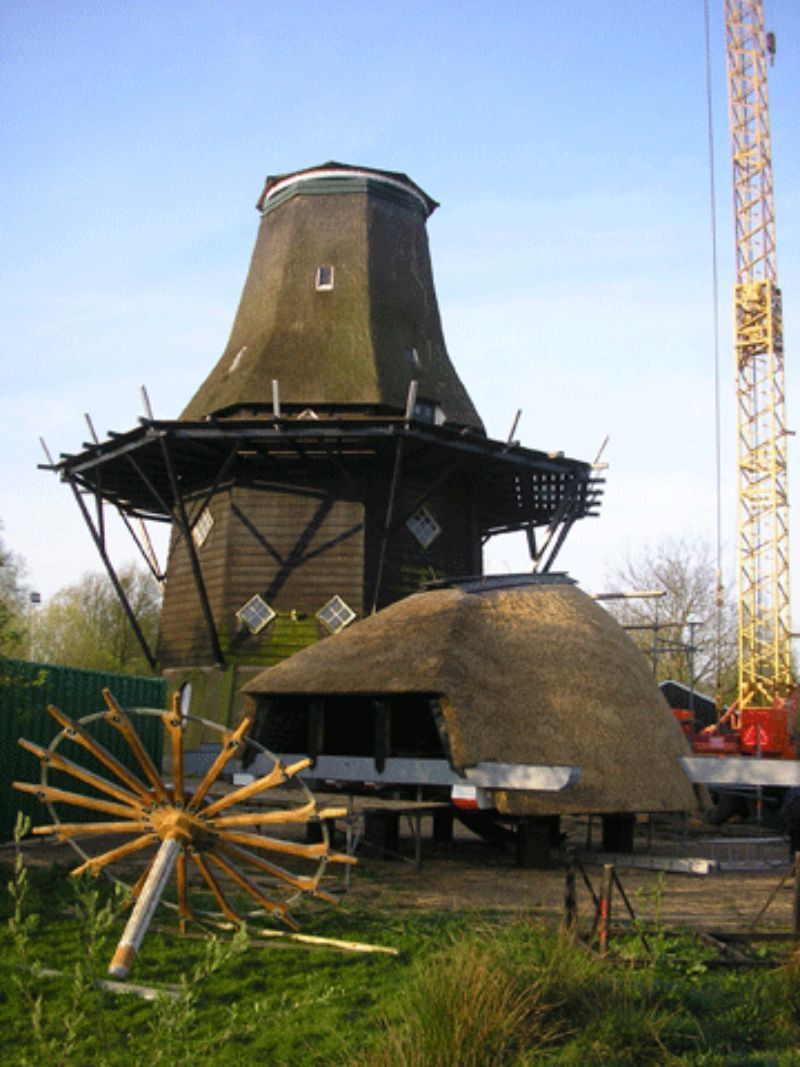 Een windmolen in aanbouw, met een nieuw rieten dak, een houten frame en een kraan ernaast.