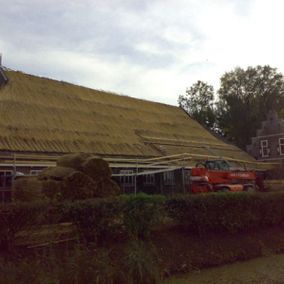 Gebouw in aanbouw met een rieten dak, met een rode vrachtwagen en zichtbare bundels riet.