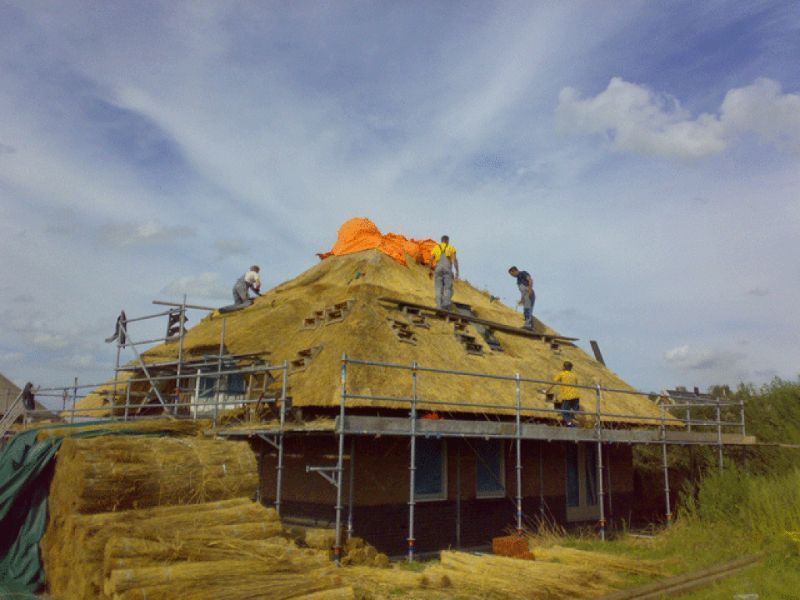 Bouwvakkers bedekken het dak van een gebouw met steigers en stapels strobalen.
