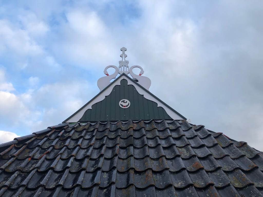 Donker pannendak van een gebouw met een witte decoratieve puntgevel tegen een bewolkte lucht.