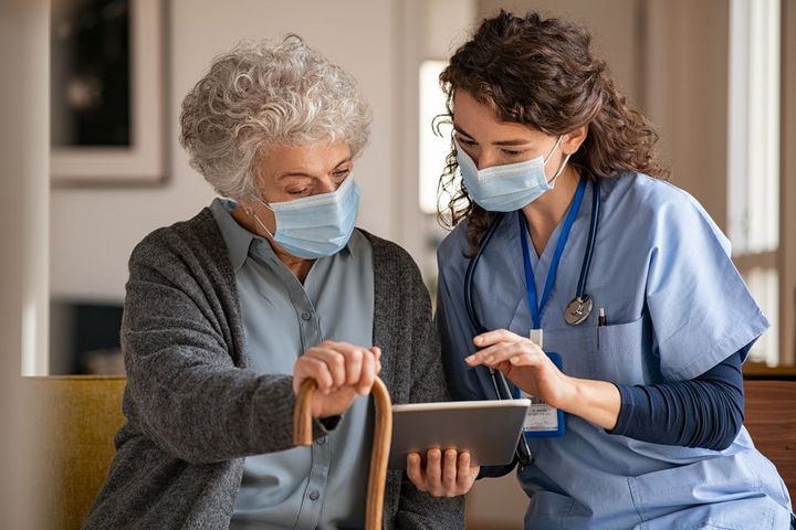Woman with cane and medical professional looking at a tablet, both wearing masks.