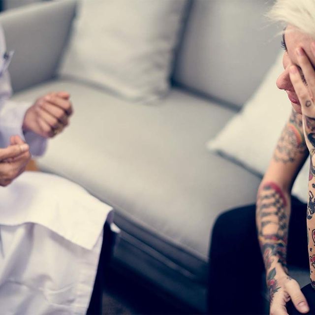 a woman with tattoos is sitting on a couch talking to a doctor .