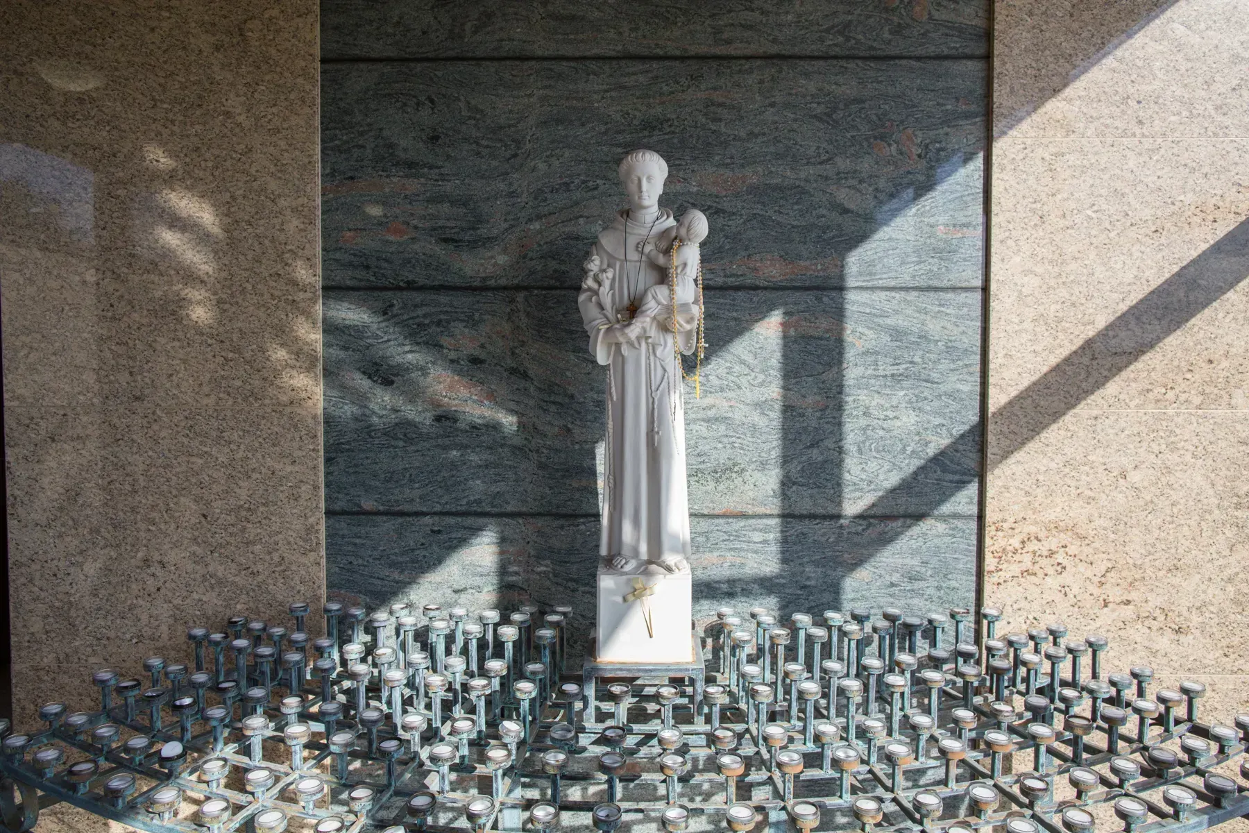 Statue in a memorial alcove, surrounded by rows of lit votive candles