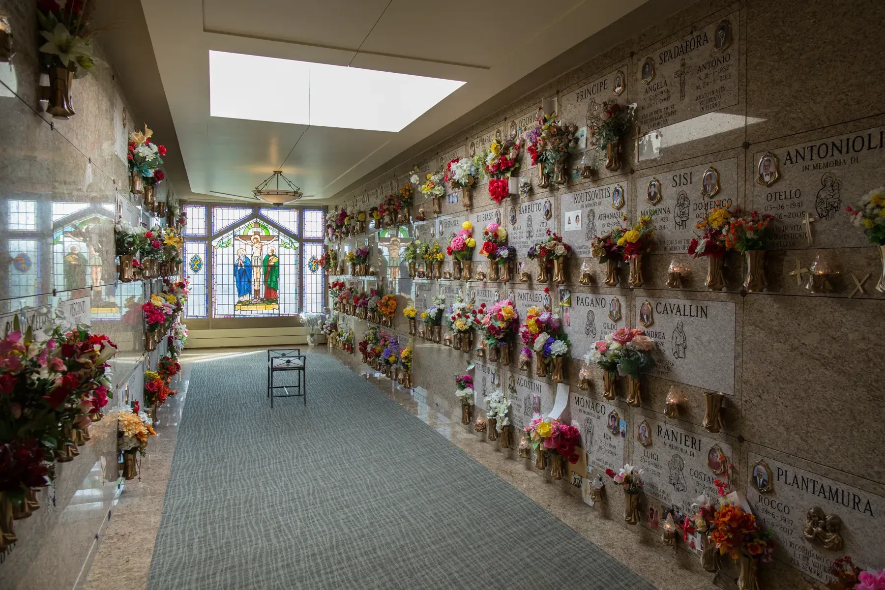 Hallway lined with memorial flower arrangements, with a stained-glass window at the end