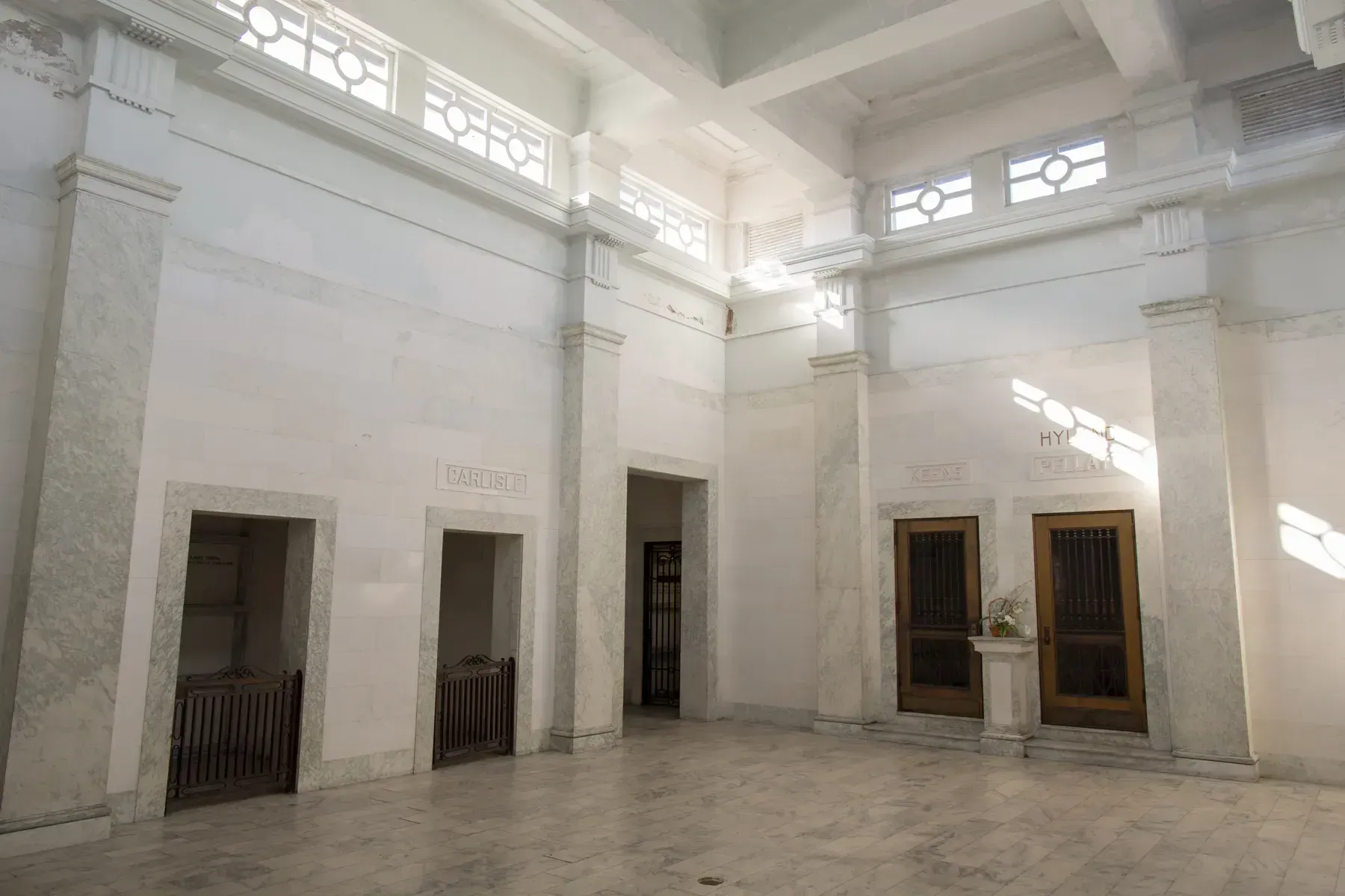 Bright white courtyard with tall columns, doorways, and sunlight streaming across the stone floor
