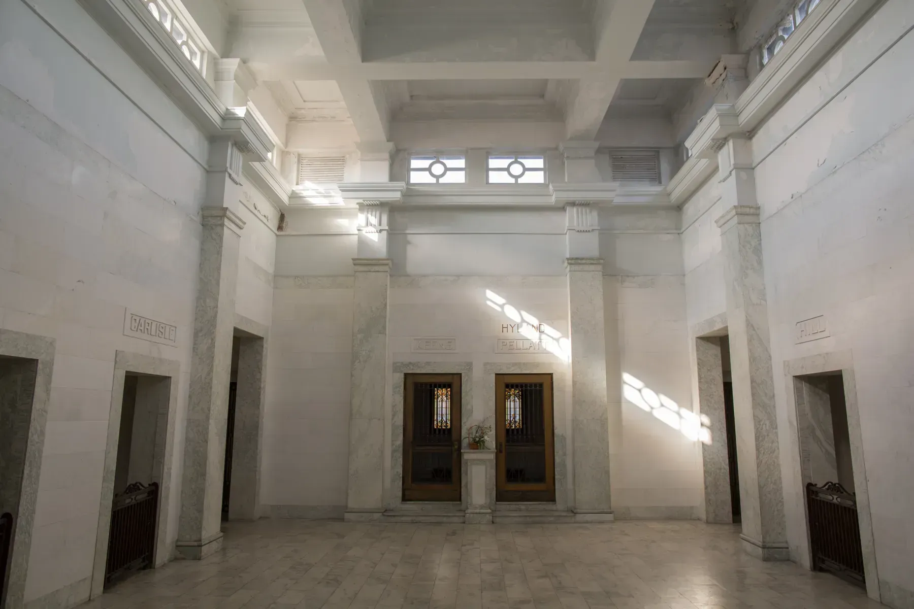 Bright white marble interior hall with tall columns, high windows, and double doors centered on the far wall