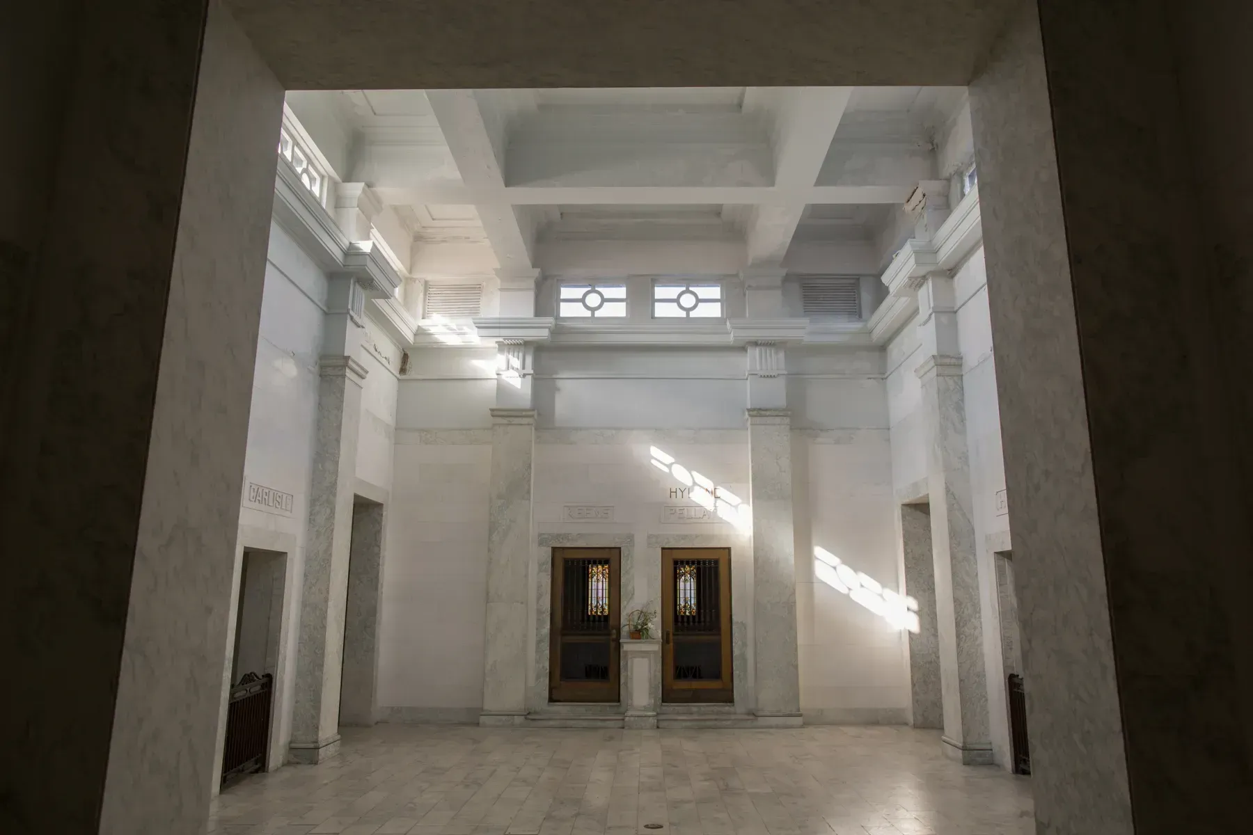 Empty white interior hall with tall columns, high windows, and sunlight streaming in