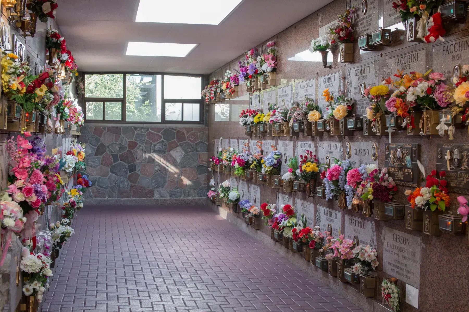 Indoor columbarium wall lined with colorful flower arrangements and memorial plaques