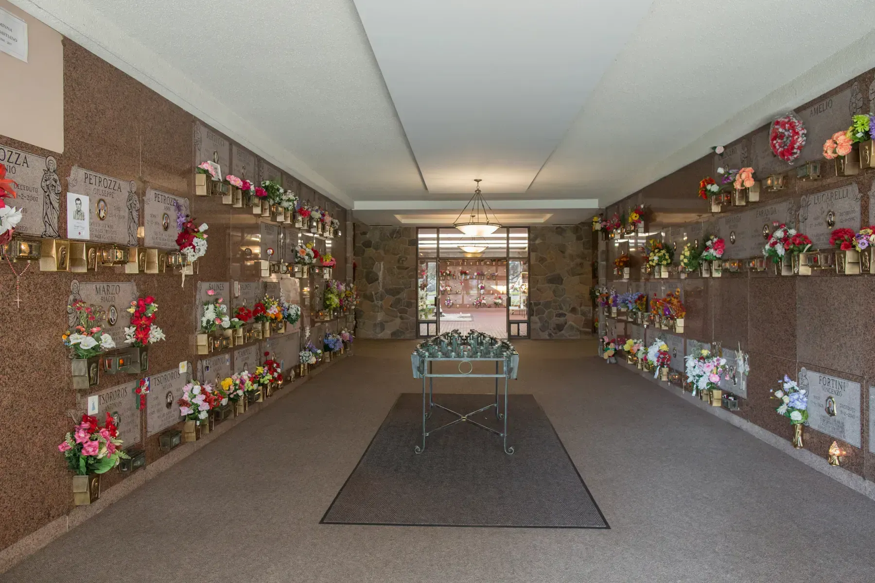 Flower-lined indoor funeral corridor with a central table and carpeted aisle