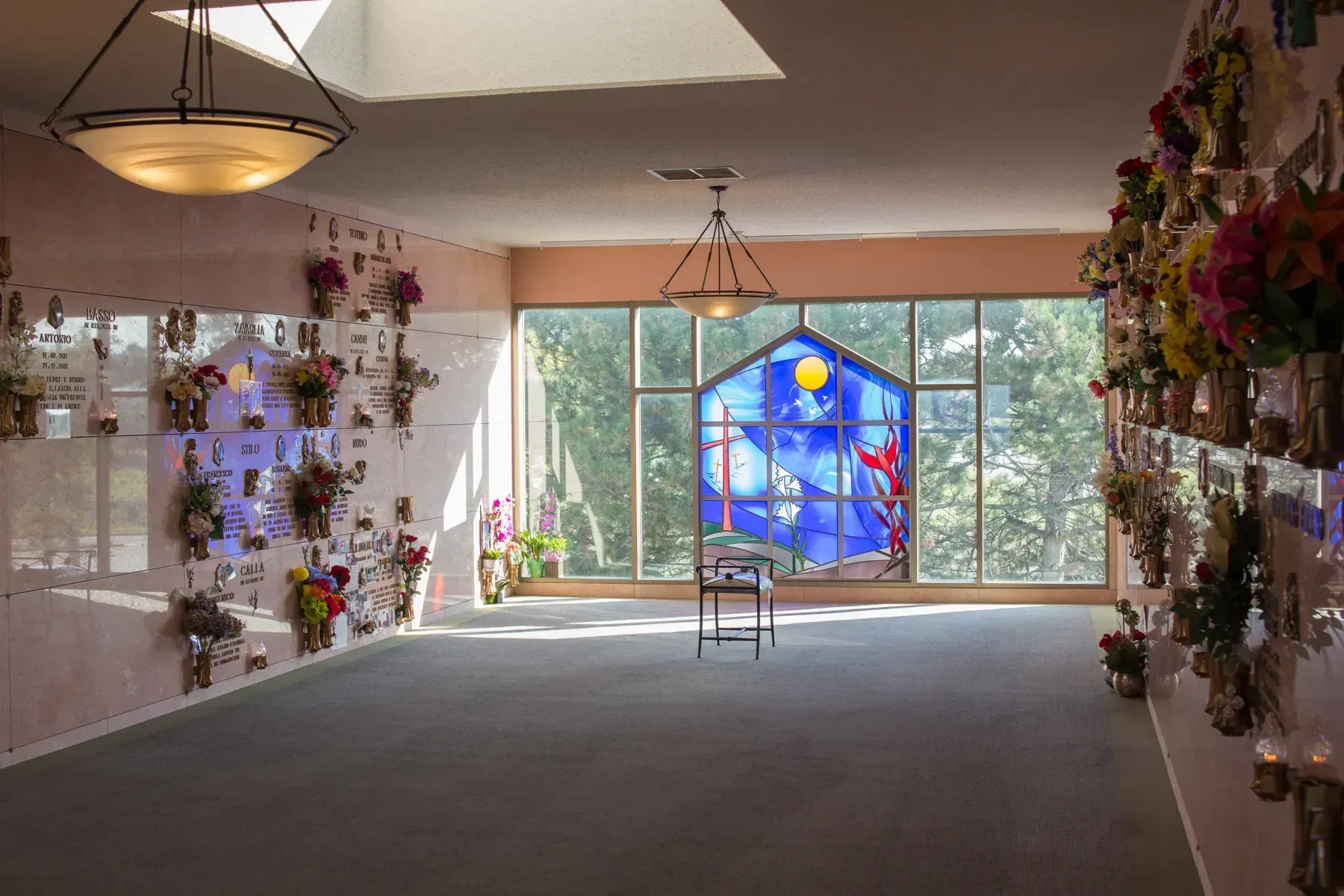 Wide gallery room with hanging floral displays and a colorful blue stained-glass window at the far end