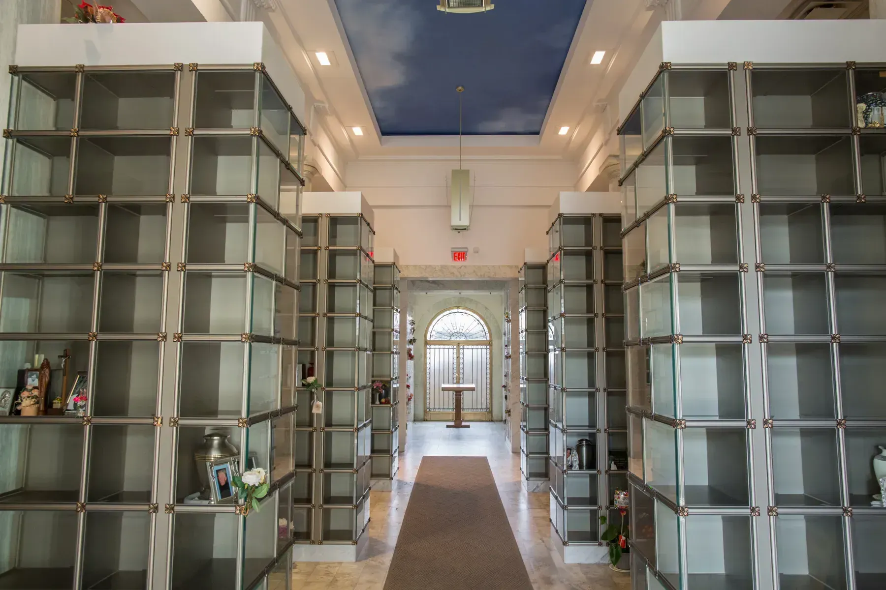 Symmetrical hallway lined with tall glass shelves and a blue-lit ceiling opening at the far end