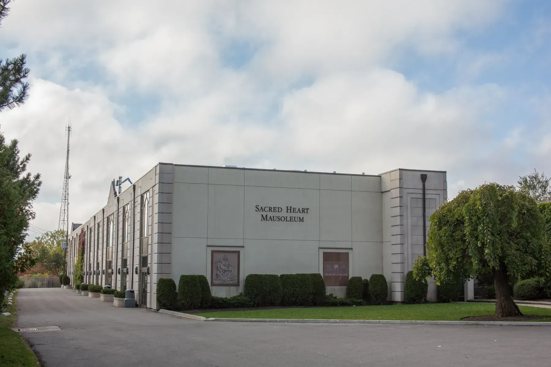 Exterior of a white church building with a sign, bushes, and a tree under a cloudy sky