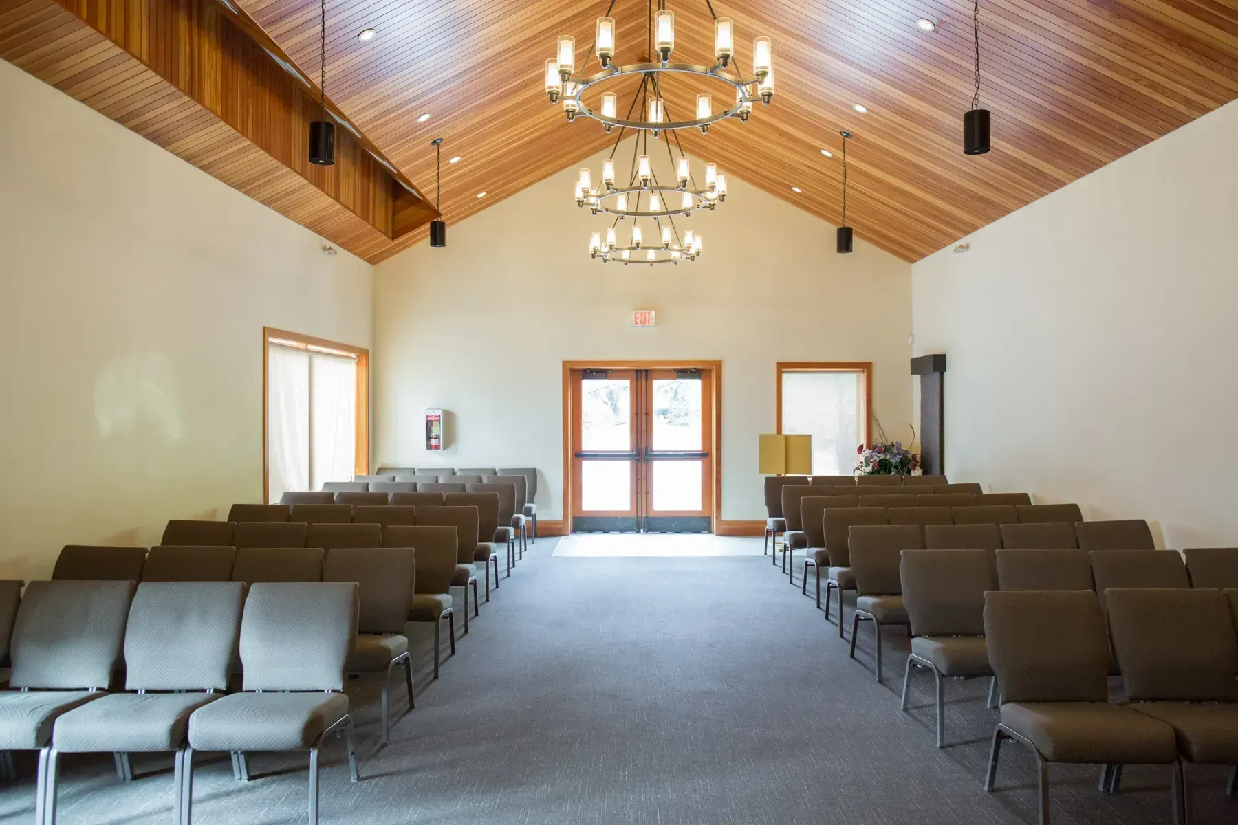 Empty church sanctuary with rows of brown chairs, chandeliers, and a wooden vaulted ceiling