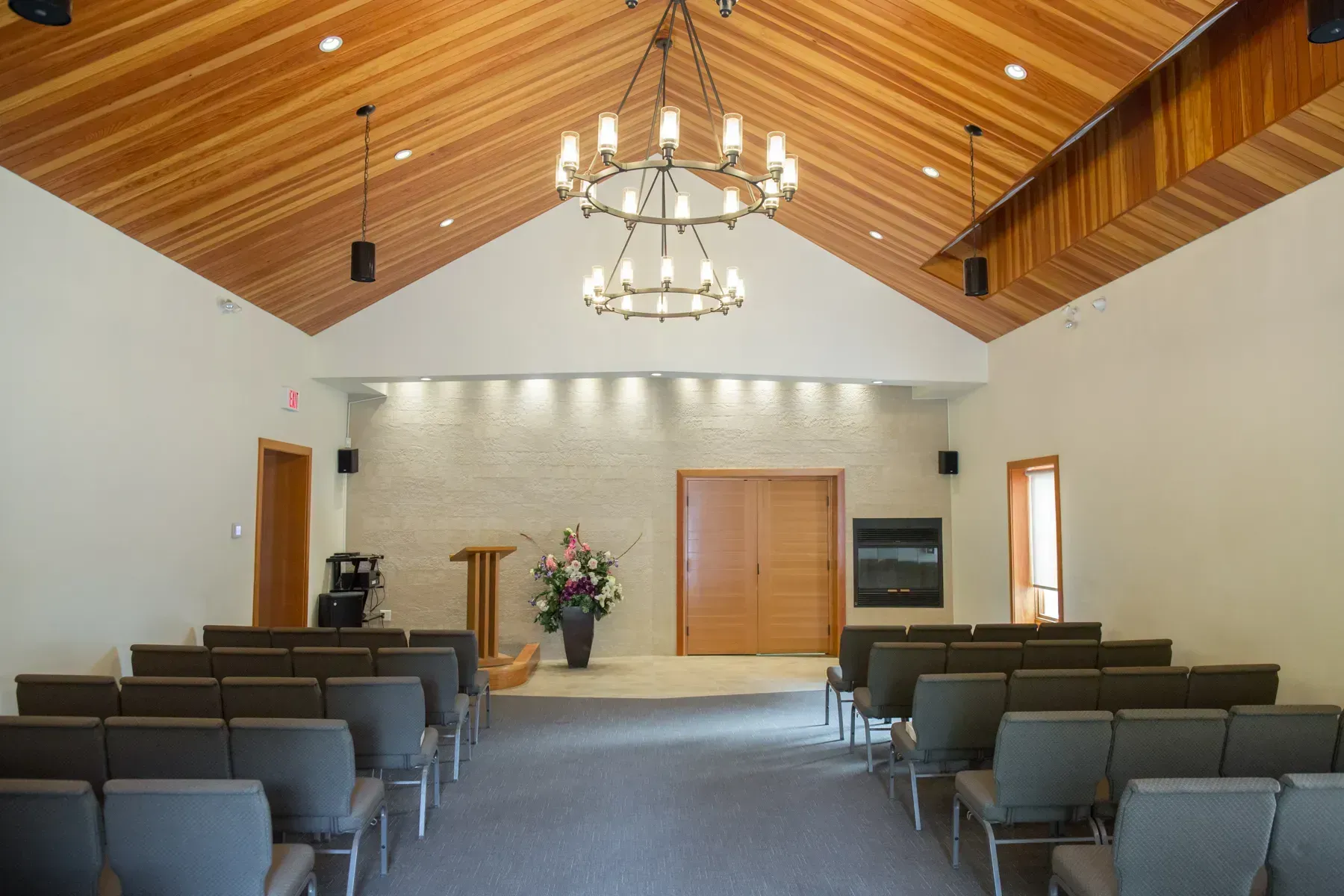 Empty chapel interior with rows of chairs, a chandelier, and a wood-paneled vaulted ceiling