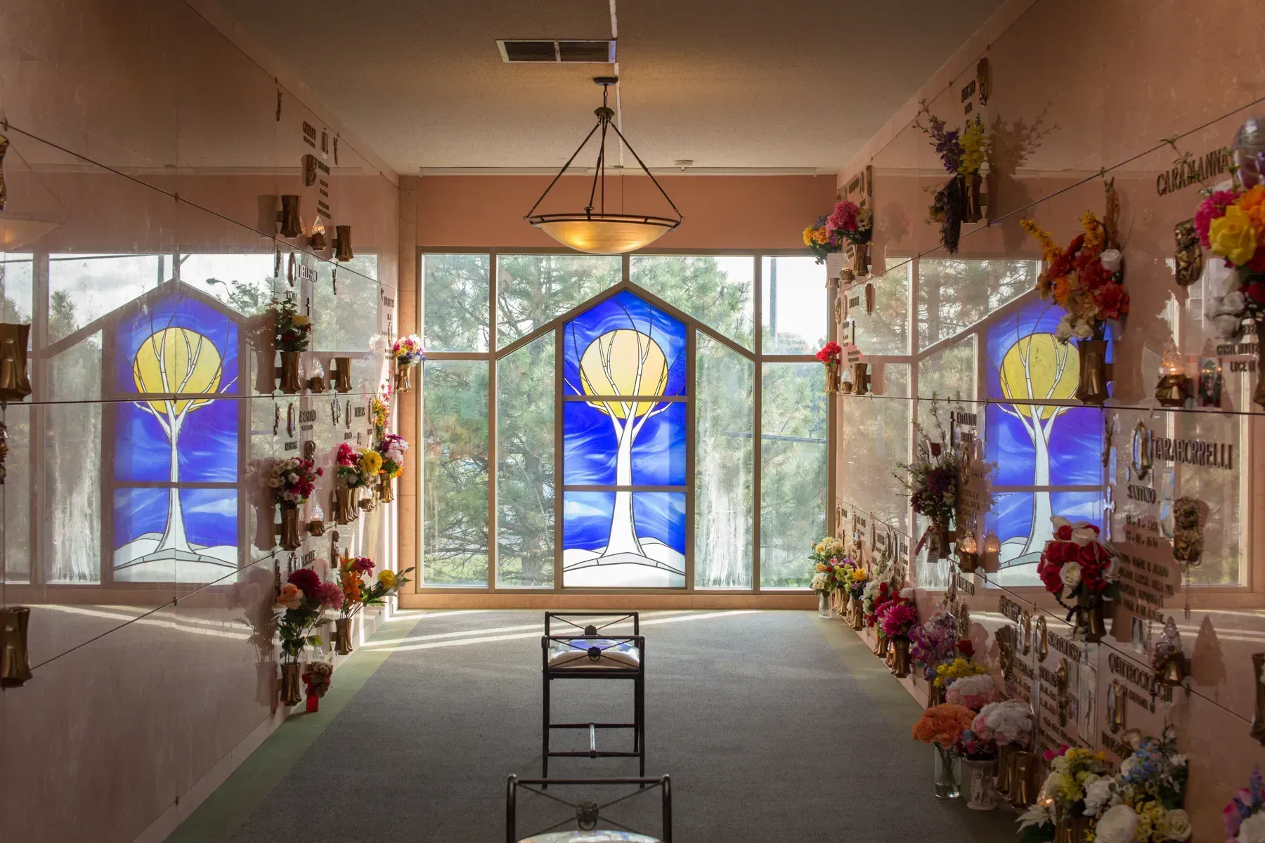 Flower-filled room with blue stained-glass windows and a hanging light over a central aisle
