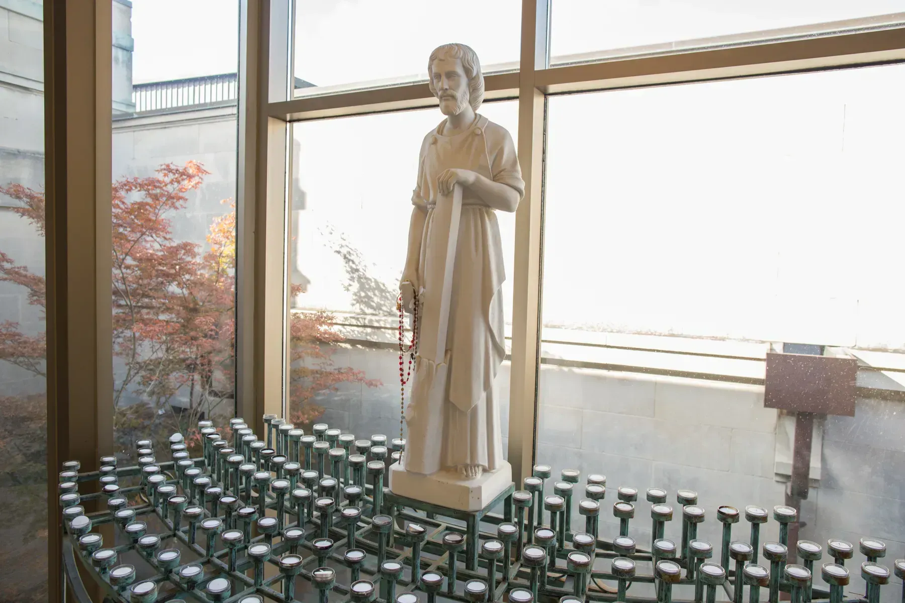 Stone statue in a chapel beside rows of lit votive candles and tall windows