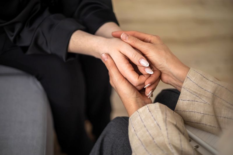 Two people holding hands in a close, comforting gesture indoors