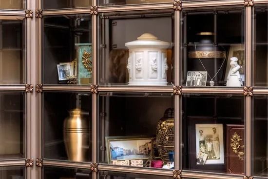 Wooden display cabinet with shelves of urns, framed photos, and decorative keepsakes