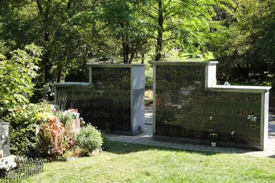 Two polished granite gravestones in a green cemetery surrounded by trees