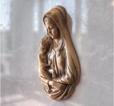 Bronze relief of a hooded woman cradling a child on a light stone wall
