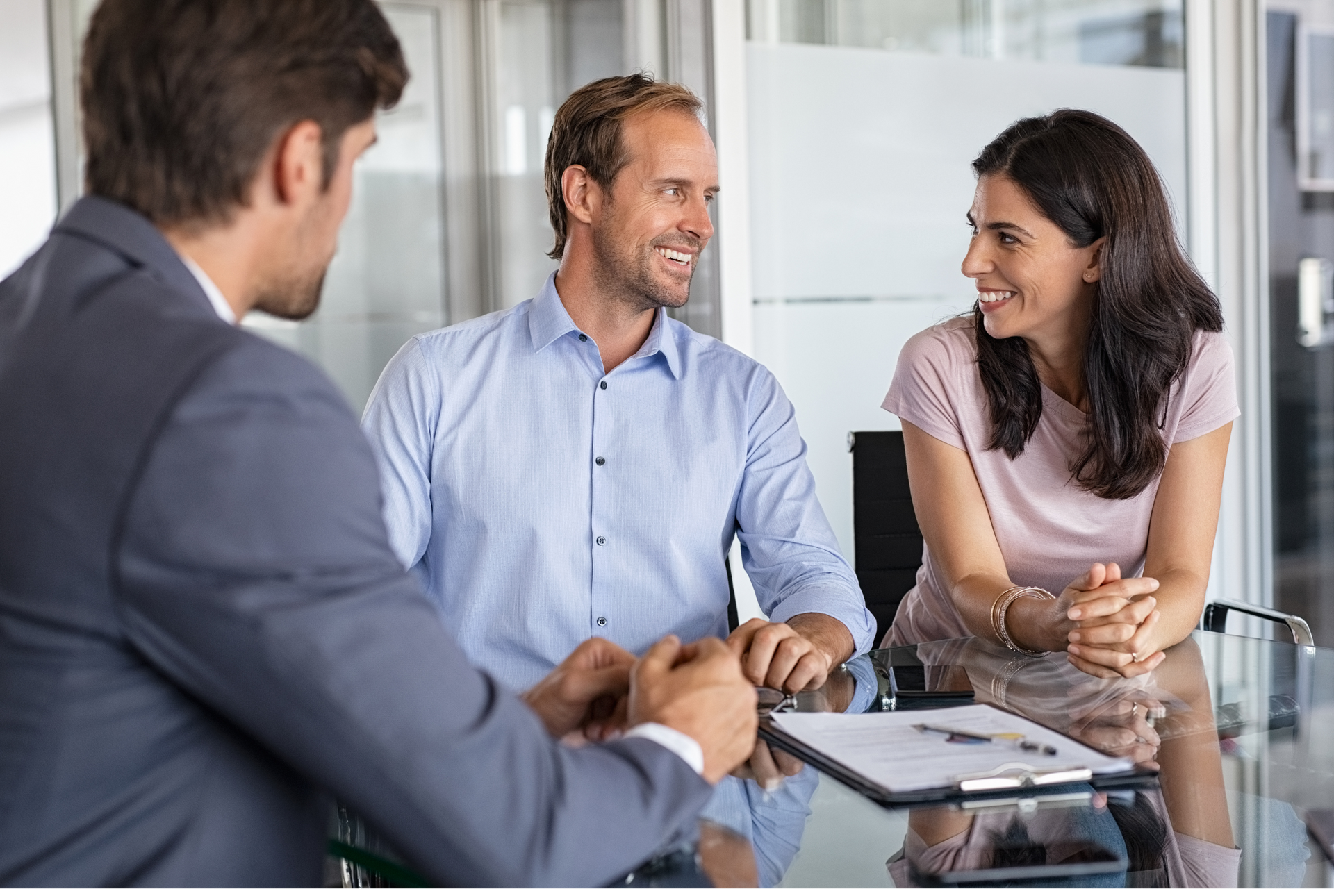 A man and a woman are sitting at a table talking to a man in a suit.