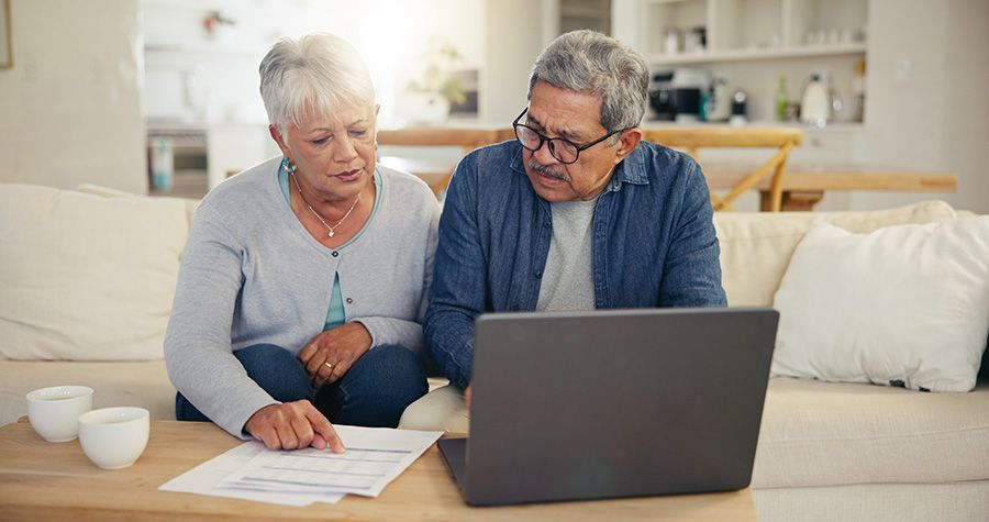 Two people reviewing documents beside a laptop on a couch in a bright living room