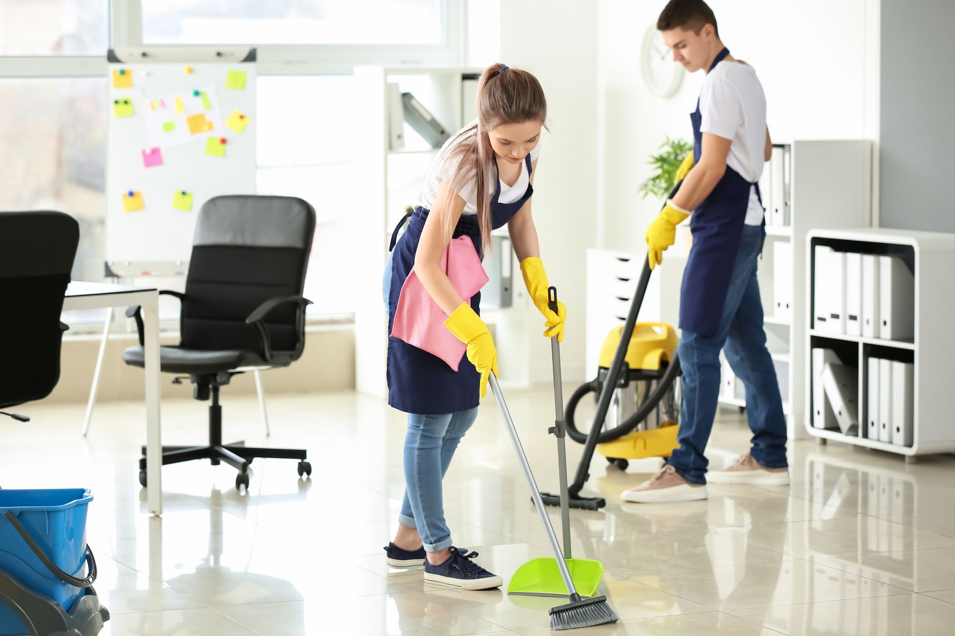 Two cleaners mopping a bright office floor with yellow gloves and a vacuum nearby