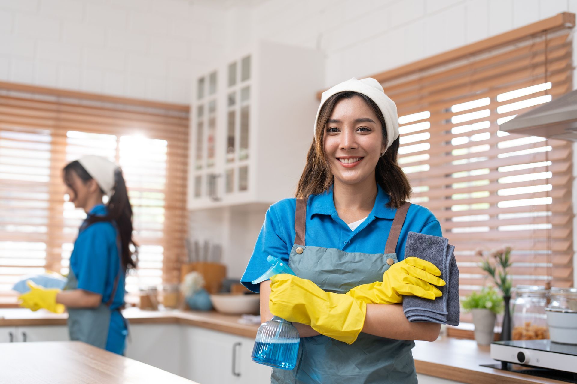 Cleaner in blue shirt and yellow gloves smiles in a bright kitchen, holding cleaning supplies.