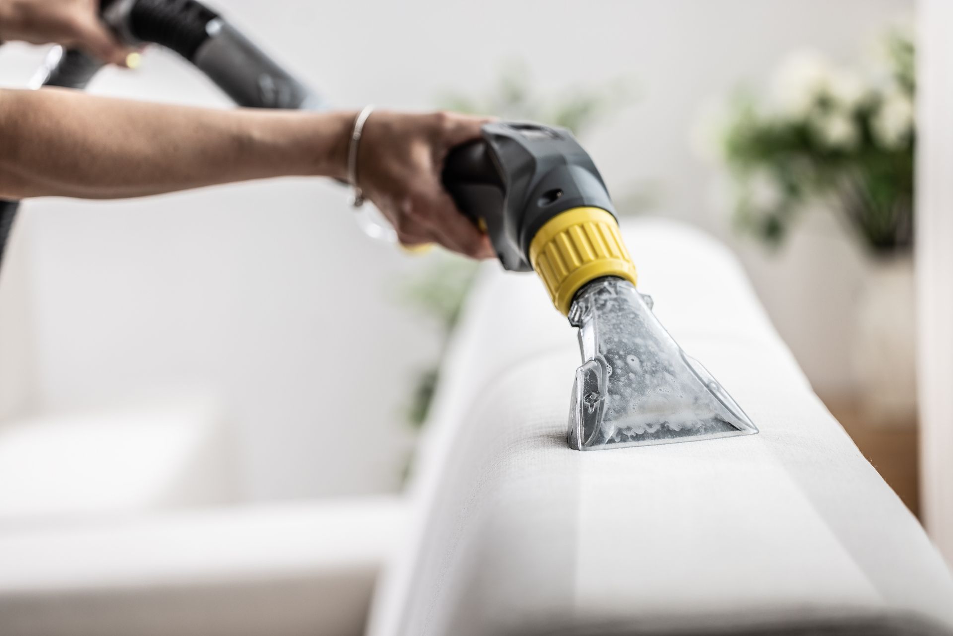 Hand using a steam cleaner on a white couch cushion, cleaning upholstery