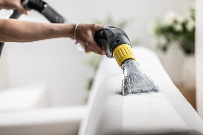 Hand using a steam cleaner on a white couch cushion, cleaning upholstery