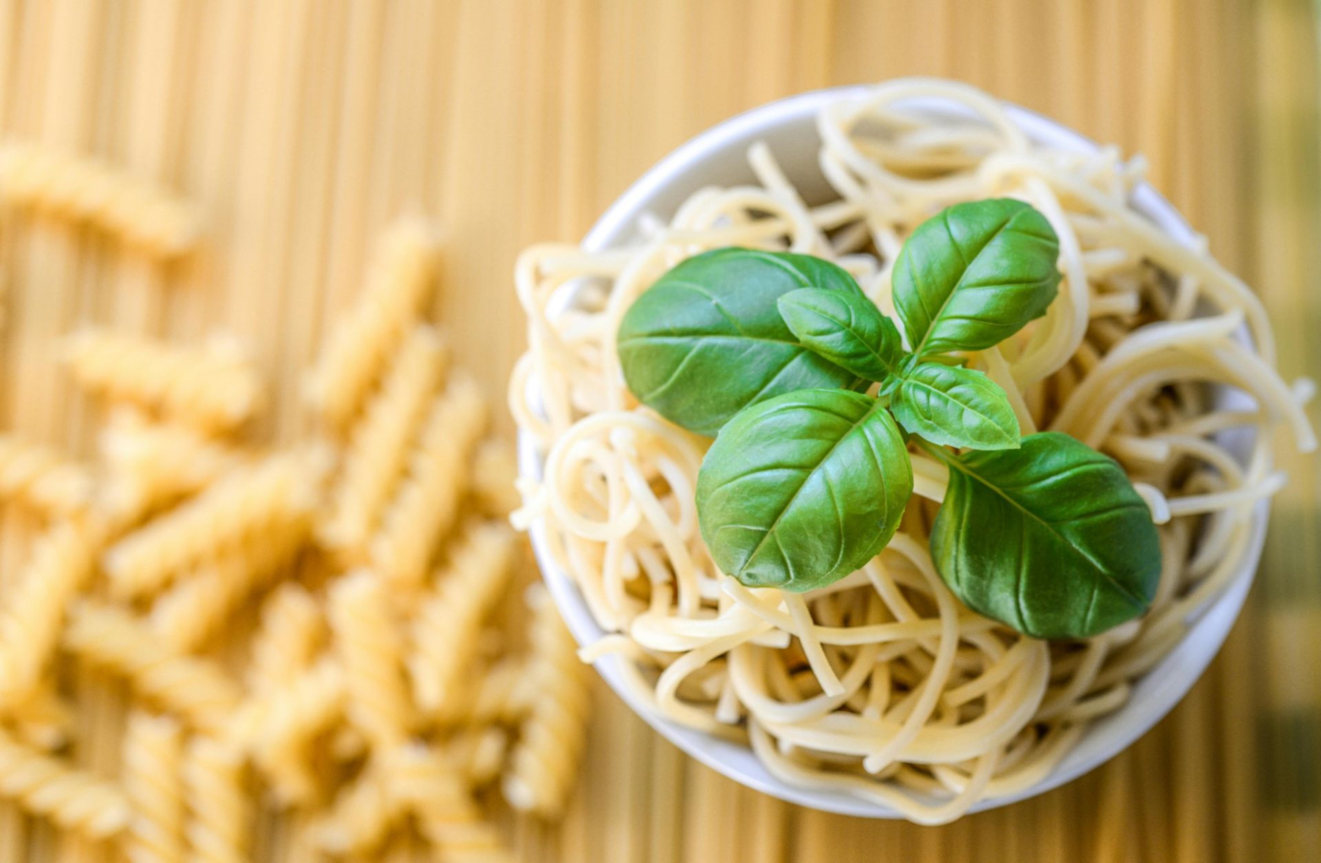A bowl of noodles with basil leaves on a wooden table.