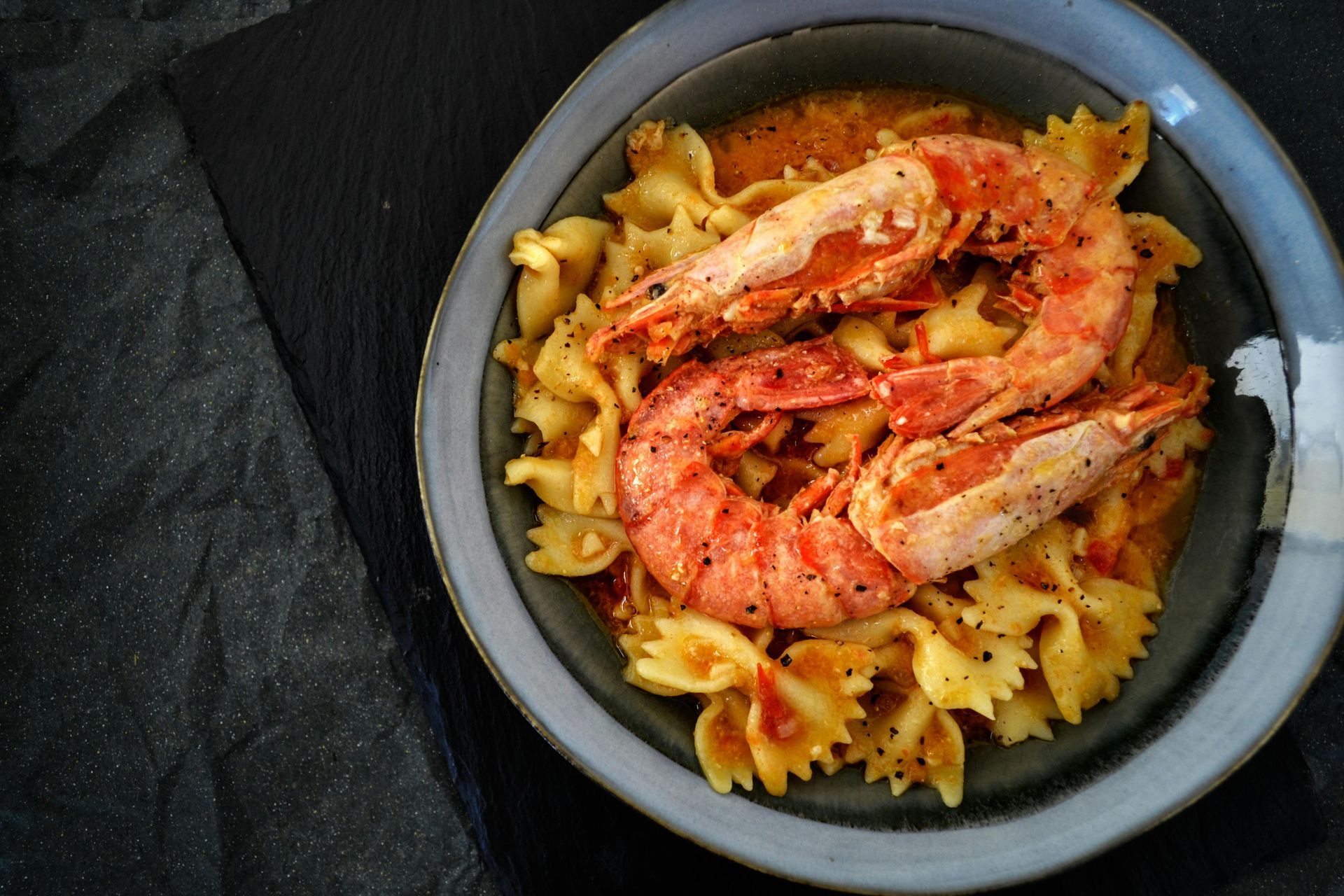 A bowl of pasta with shrimp and sauce on a table.