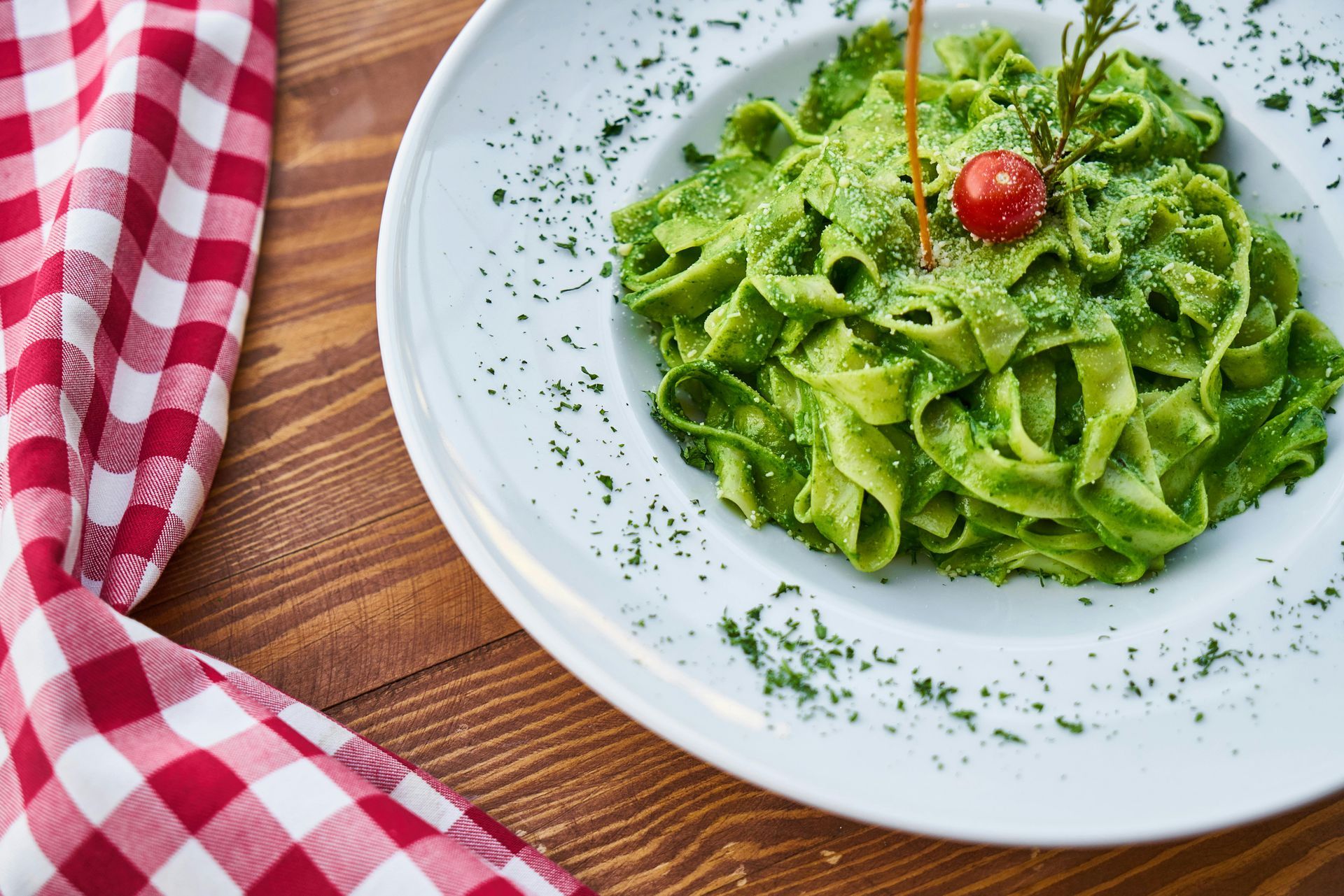 A white plate topped with green pasta and a tomato on a wooden table.