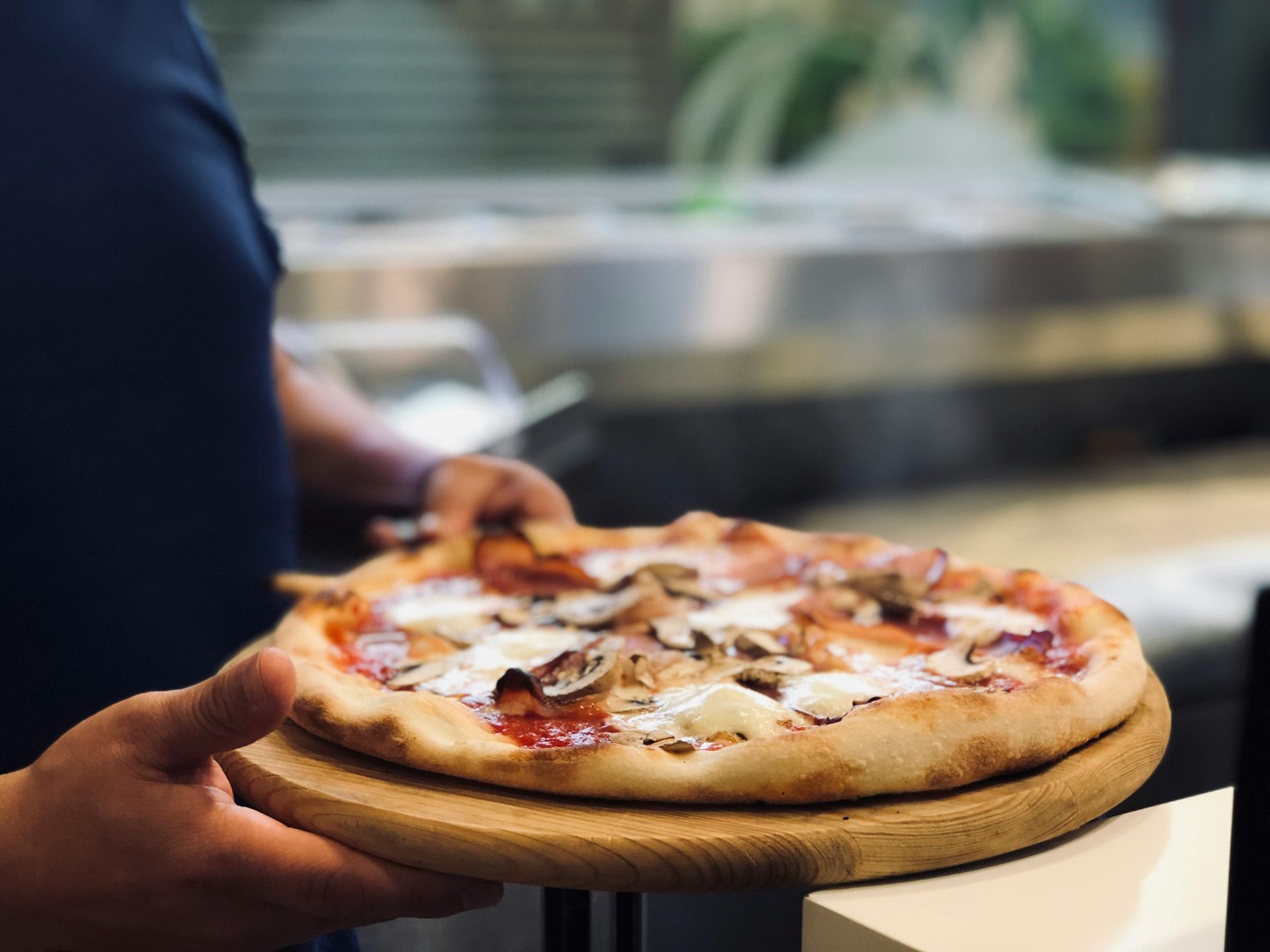 A person is holding a pizza on a wooden tray.